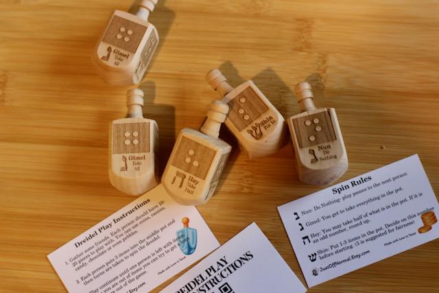 Wooden dreidel with braille letter matching the starting sound of the Hebrew letter on each side (N-Nun, H - Hey, G - Gimel, S - Shin) plus game instruction card and QR code link to audio game instructions.