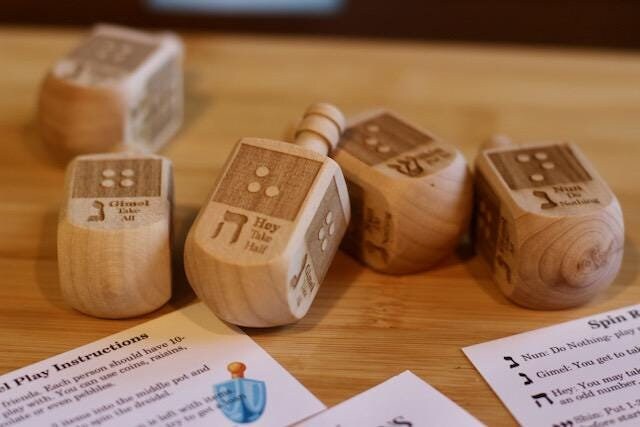 Wooden dreidel with braille letter matching the starting sound of the Hebrew letter on each side (N-Nun, H - Hey, G - Gimel, S - Shin)