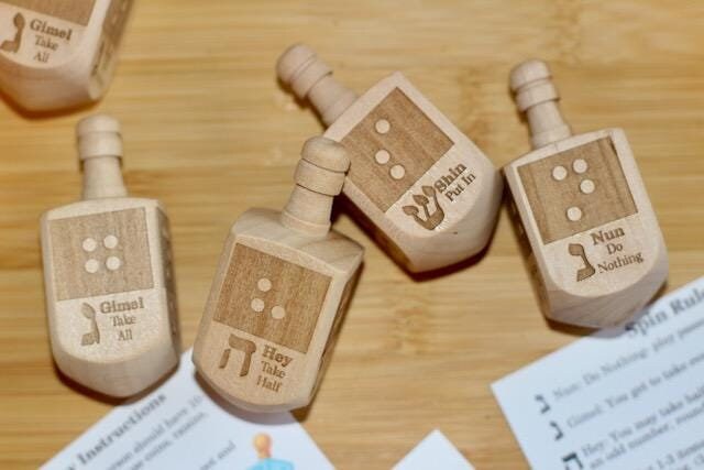 Wooden dreidel with braille letter matching the starting sound of the Hebrew letter on each side (N-Nun, H - Hey, G - Gimel, S - Shin)